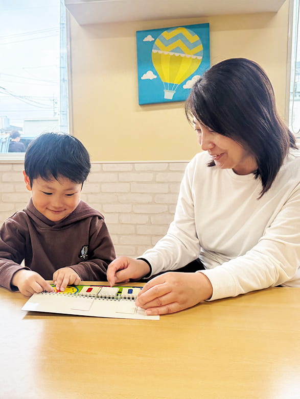 英単語が書いたボードを指さしながら子どもに指導している保育士の女性