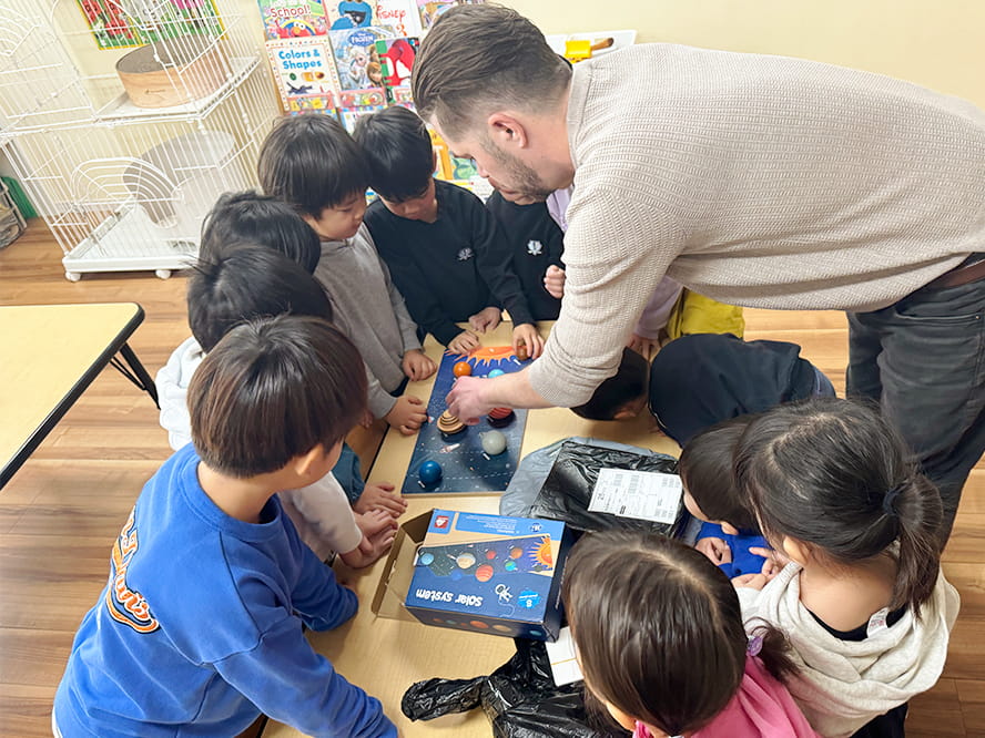 惑星の模型を使い、英語で会話をしながら授業をしている講師と生徒たち