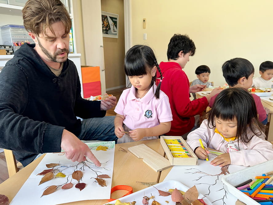 植物の葉っぱを使い紙のうえで木を作っていく授業を受けている生徒たち