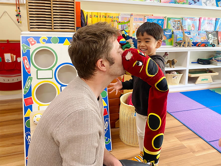 蛇のぬいぐるみをもって先生の顔にくっつけて戯れている生徒と代表の講師