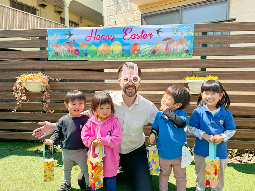 手を広げてフランクリンスクール倉敷校の庭で生徒と笑顔で微笑む代表の講師