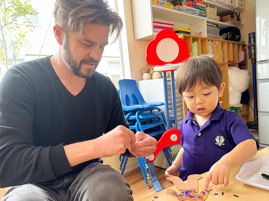 英語で会話をしながら、折り紙を貼って人形を作っていくフランクリンスクール倉敷校の代表と生徒