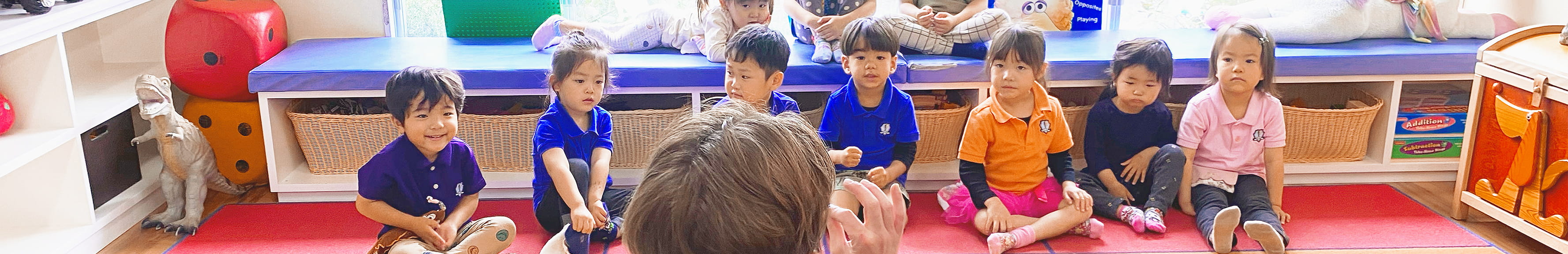 カラフルなマットを敷いた教室で、英会話のレッスンを受けている子供たちの様子