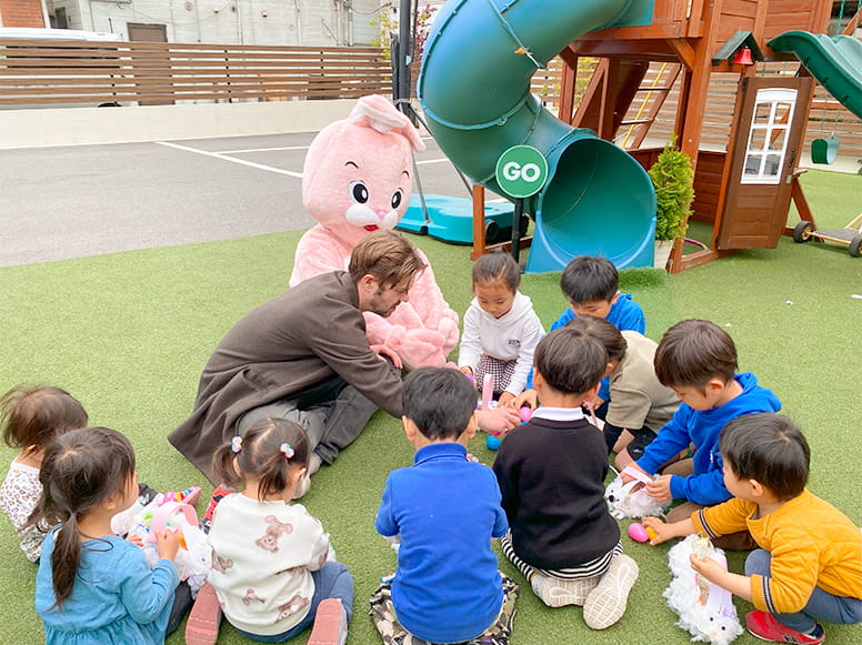 フランクリンスクール倉敷校の広い敷地内で生徒に囲まれてレッスンをする講師と着ぐるみのウサギ